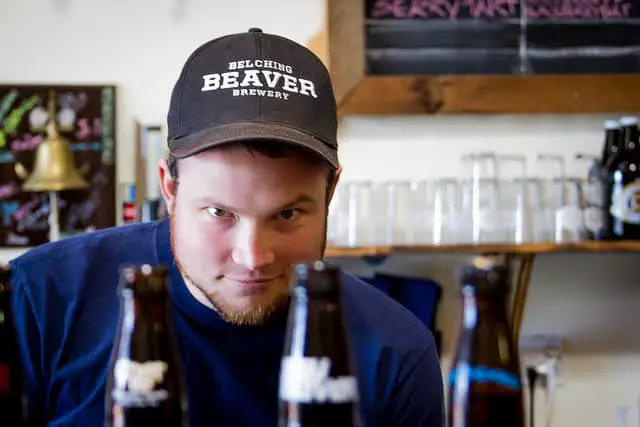 Man Wearing Black Cap Looking at the Three Bottles of Available Drinks at the Belching Beaver Brewery